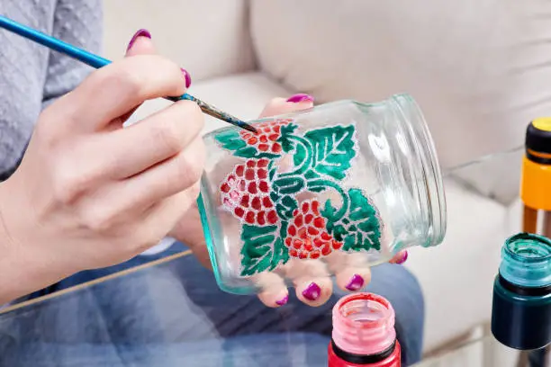 Photo of A girl paints a glass jar with stained glass paints