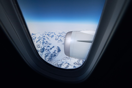 View from airplane window during flight above snowcapped mountains of Greenland.\