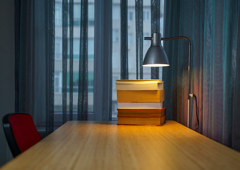 Small light bulb glowing on the desk, with notebook and many books on background, reading and writing idea concept