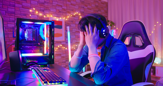 asian male esport gamer plays exciting online game in room with neon lighting - he lost and feels upset
