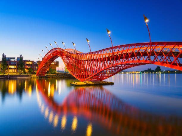 eine brücke in der stadt bei nacht. die brücke auf dem blauen himmelshintergrund während der blauen stunde. architektur und design. the python bridge, amsterdam, niederlande. - architecture bridge built structure business stock-fotos und bilder