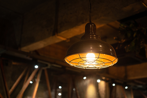 A retro style metal ceiling lighting lamp with warming light glowing bulb. Interior decor, selective focus object.