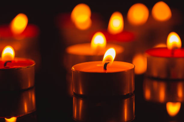Christmas backgrounds: three red burning Christmas candles shot on rustic wooden table. The composition is at the left of an horizontal frame leaving useful copy space for text and/or logo at the right.String light and Christmas decoration are out of focus at background. Predominant colors are red and brown. High resolution 42Mp studio digital capture taken with SONY A7rII and Zeiss Batis 40mm F2.0 CF lens