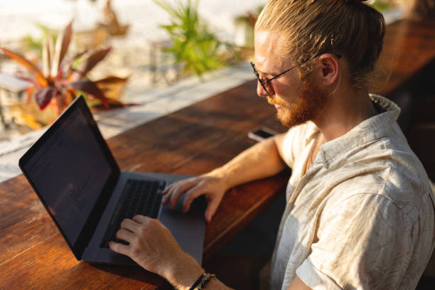 istock Young Caucasian male freelancer working on laptop, from the beach bar 1402475268