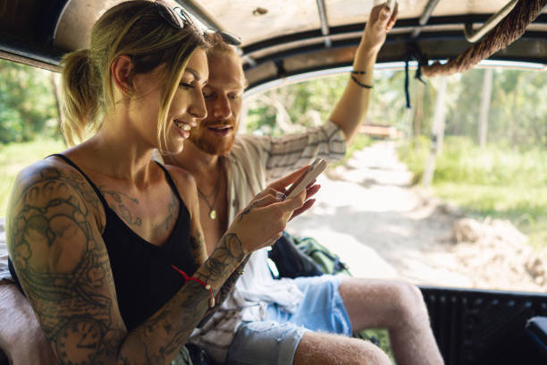 While exploring the island with taxi, modern young couple using mobile phone Young Caucasian couple travel together, in the off road taxi, during their vacation while using mobile phone tourist couple candid travel stock pictures, royalty-free photos & images