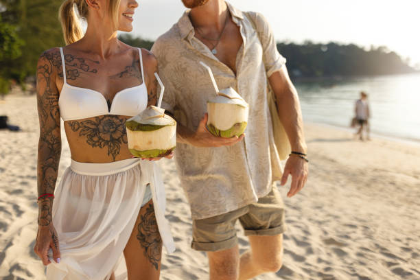 istock Unrecognizable Caucasian couple walking on the beach and drinking coconut 1402475701