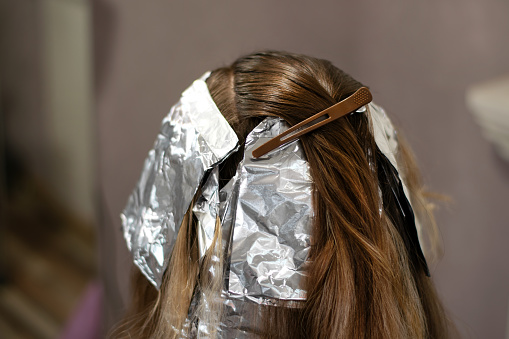Making highlights with the help of sheet of foil. Dyeing long hair of the female client in the beauty shop. Rear view