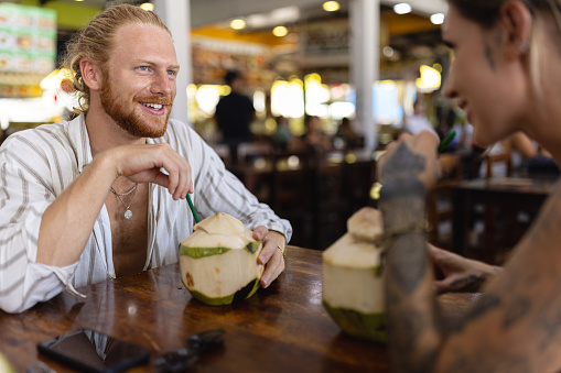 Young Caucasian couple drinking coconut at the modest restaurant, while travel together