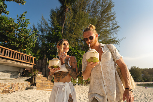 Caucasian couple drinking coconut on the beach, during their vacation