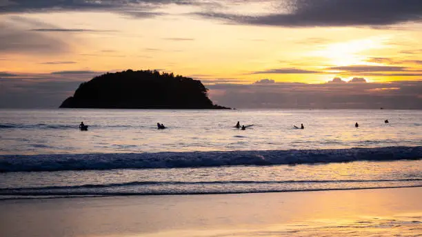 Surfers sitting on surfboard in water at the beach with sunset. Kata Beach, Phuket, Thailand.