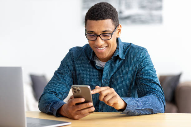 istock Young African American man entrepreneur in modern office looking at screen typing message with mobile phone Smiling male in workplace using smartphone search the Internet or chatting in social network 1402490855