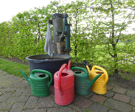 Colourful watering cans next to a water pump. Seen in a cemetery in Germany