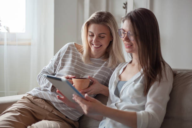 istock Two young women friends using tablet together, sitting on the couch smiling and fun 1402495905