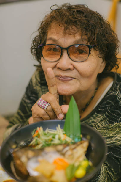 a velha asiática câmera de rosto de rosto sorrindo em mãos mostrando comida local ou comida japonesa. uma mulher envelheceu e lhe mostrará sushi e pães. - 11193 - fotografias e filmes do acervo
