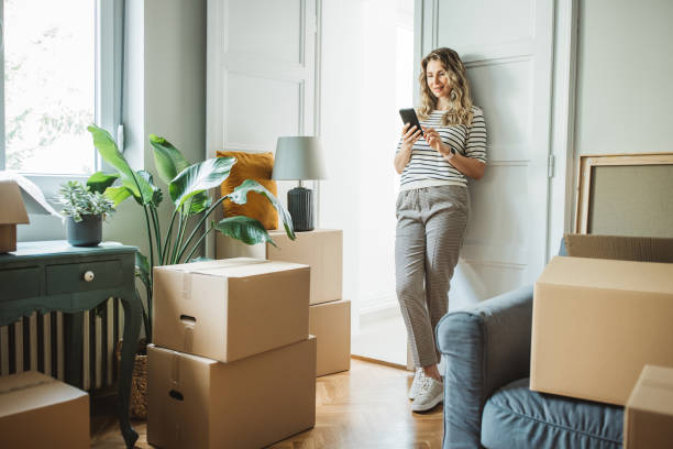 Mature woman with Moving Boxes in New Home Mature woman moves in to new home, unpacking boxes and enjoying in her new home. She is resting and using smart phone. fresh start stock pictures, royalty-free photos & images