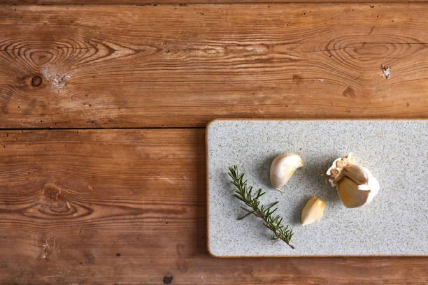 Overhead view of freshly cut garlic cloves with branch of seasoning rosemary herbs on chopping table over wooden table