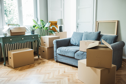 Moving day concept, cardboard carton boxes stack with household belongings in modern house living room, packed containers on floor in new home.