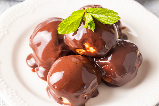 Delicious profiteroles with chocolate and white plate. Selective focus image on light background.