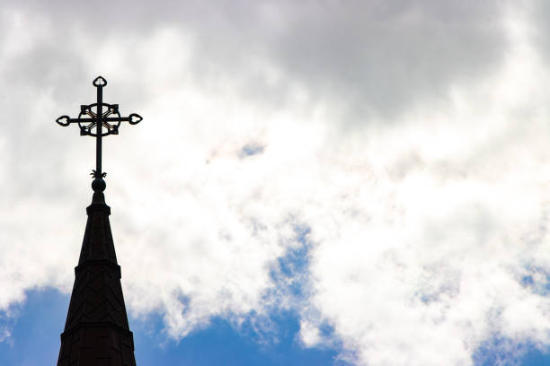 A black silhouette of a Christian church cross and steeple on the left against a cloudy sky.