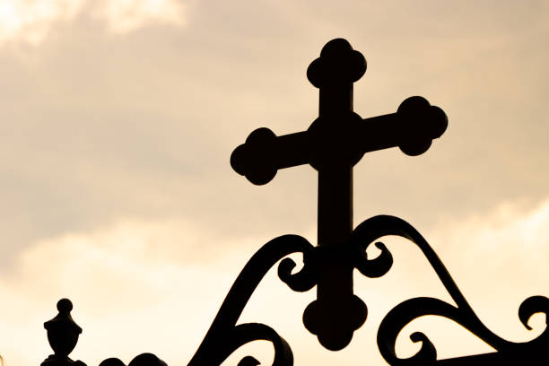 The silhouette of a decorative Christian cross on a fence near sunset.