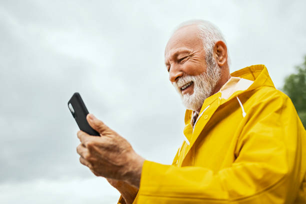 istock Senior man walking on a raining day using smart phone 1402507541