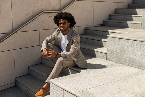 Portrait of good-looking Black man outdoors. African American man in suit sitting on stairs.  Portrait, city life concept