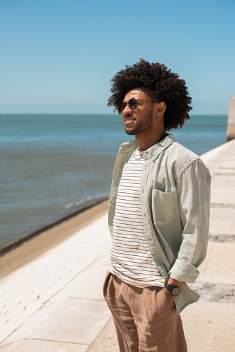 Tranquil African American man walking on embankment. Stylish man in casual clothes having walk on summer day. Relaxation, leisure concept