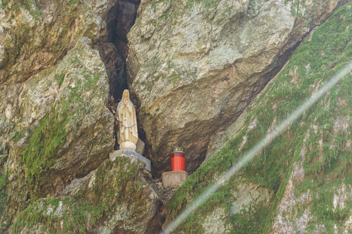 Small statue of holy mary mother god in rock crevice with red candle in front in a forest