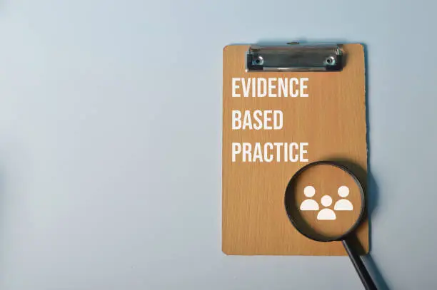 Magnifying glass and wooden clipboard with text EVIDENCE BASED PRACTICE
