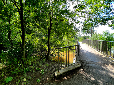A bicycle and pedestrian bridge over a small dirty river.