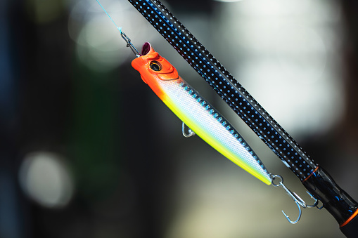 fishing bait lure hanging on a threefold hook. glow brightly colored fake fish\non blury background