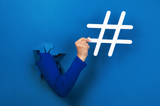 hand holding hashtag sign over blue background, social media concept