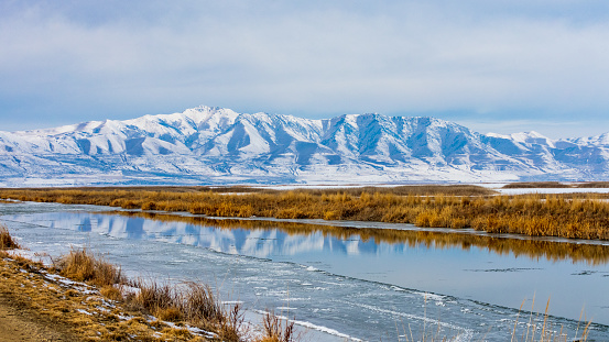 Snow covered mountains reflect in partially frozen water in Bear River Migratory Bird Refuge, Utah