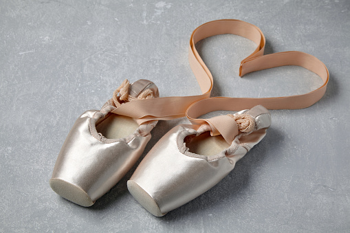 Beige pointe shoes with ribbons laid out in the shape of a heart on a light gray concrete table. Ballet shoes