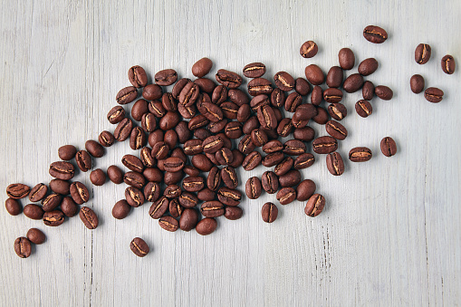 Randomly scattered roasted coffee beans on a white wooden background. Top wiev with copy space. Flat lay