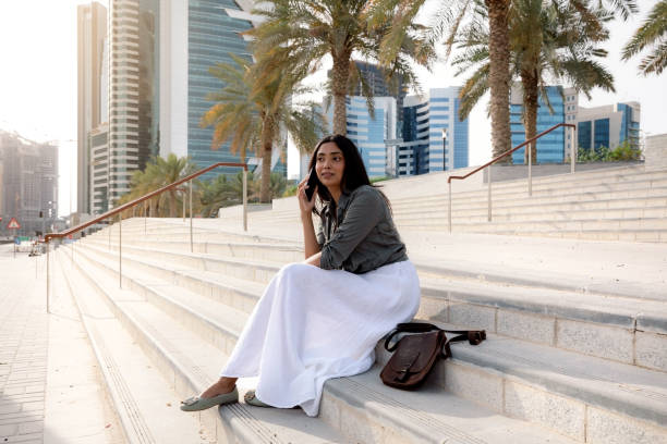 portret młodej kobiety siedzącej na schodach i rozmawiającej przez telefon w ładny słoneczny letni dzień w centrum doha - sunny cheerful close up outdoors zdjęcia i obrazy z banku zdjęć