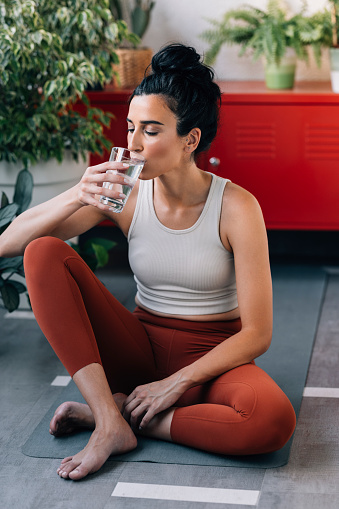 Vertical photo of a woman drinking water after her yoga practice.