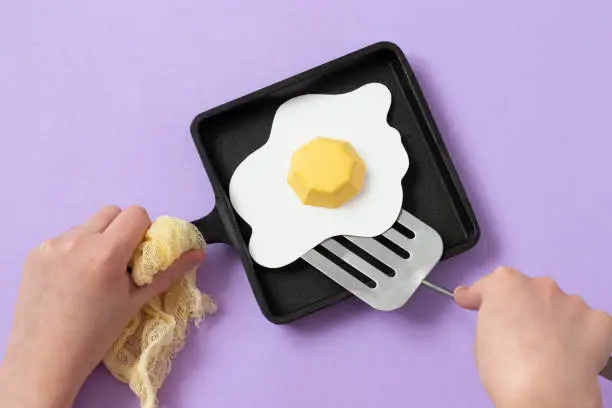 Hands holding a cast-iron frying pan with paper fried eggs. Realistic handmade paper objects. Paper art and craft. Minimal art food concept