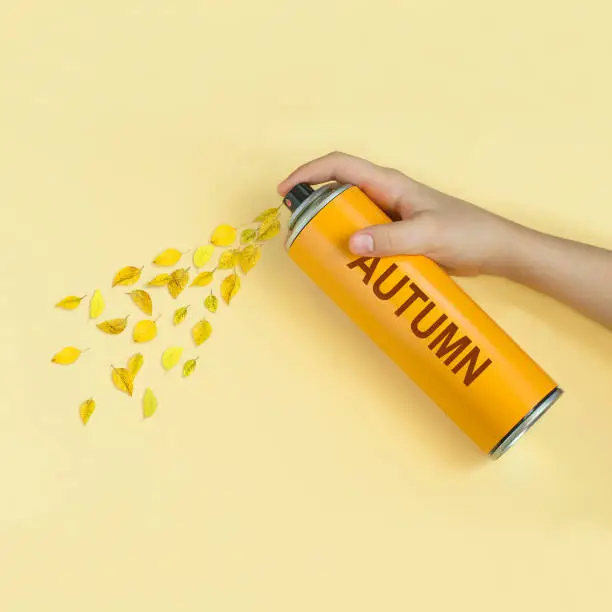 Yellow leaves fly from spray can with inscription: autumn. Yellow pastel paper background. Minimal style. Creative idea, imagination and fantasy. Original autumn concept