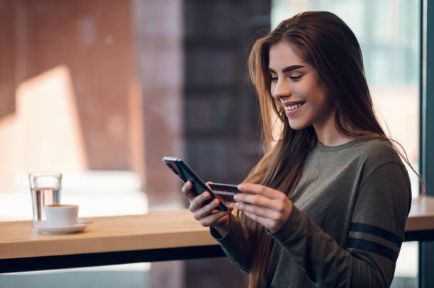 Woman using smartphone and a credit card for online shopping in a cafe stock photo