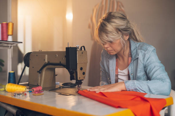 istock Tailor woman sitting and sewing on a sewing machine a in studio 1402535575