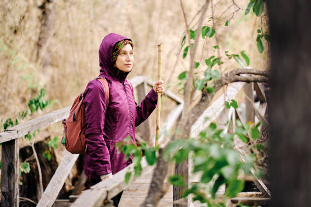 istock Woman with backpack and jacket hiking in the forest outdoors stops on a bridge 1402540138