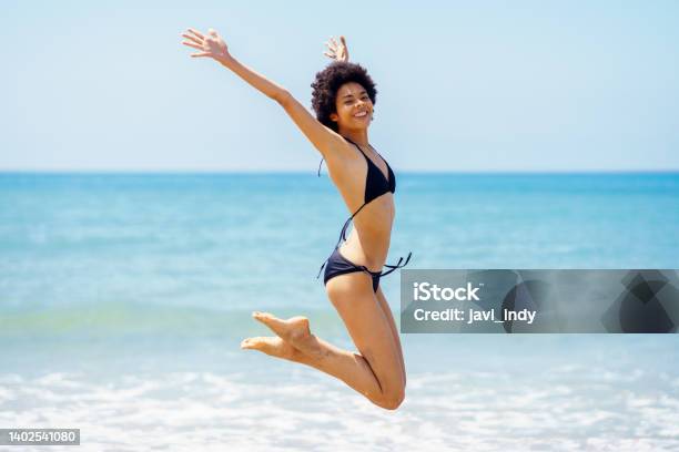 Happy Black Woman Jumping Near Sea In Summer Stock Photo - Download Image Now - One Woman Only, Women, Swimwear