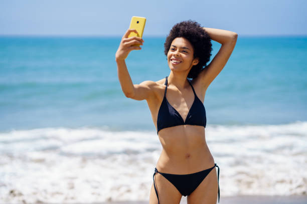 istock Content black woman in bikini taking selfie on beach 1402541084