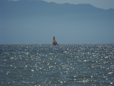 Shimmering water, blue tinted mountains and a rainbow colored sailboat on the Bay of Flags in Puerto Vallarta, Mexico.