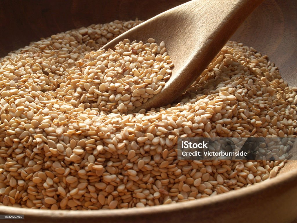 Close-up of a wooden spoon and bowl containing sesame seeds Wooden bowl of sesame seeds Sesame Seed Stock Photo