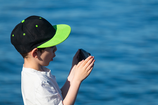 A boy films a ship's departure from port.