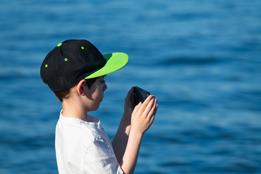 A boy films a ship's departure from port.