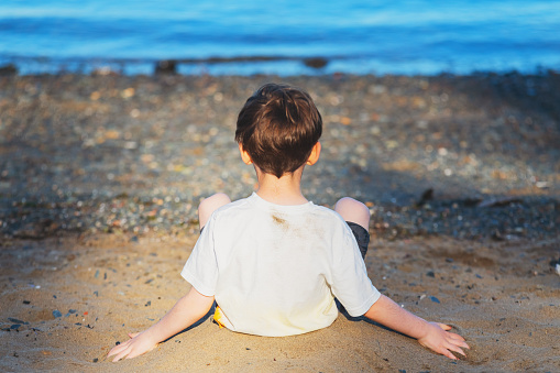 A seven year old boy buries himself in sand.