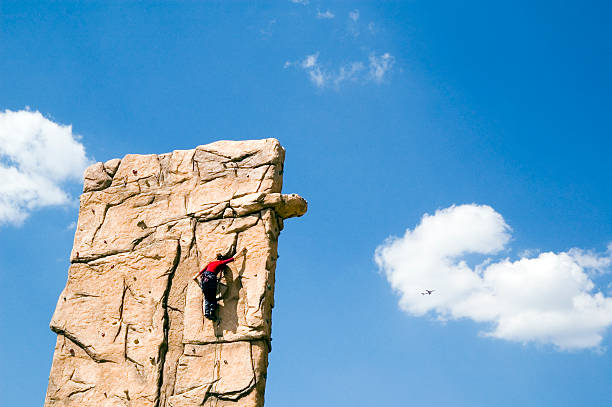 A young woman climb a climbing wall. It is secured by rope, which leads by certain safeguarding points, against a crash. The climbing wall is located in Berlin in the scene quarter “Prenzlauer Berg” in Germany. The photo developed coincidentally during a waiting period bypass in the wonderful summer 2006.